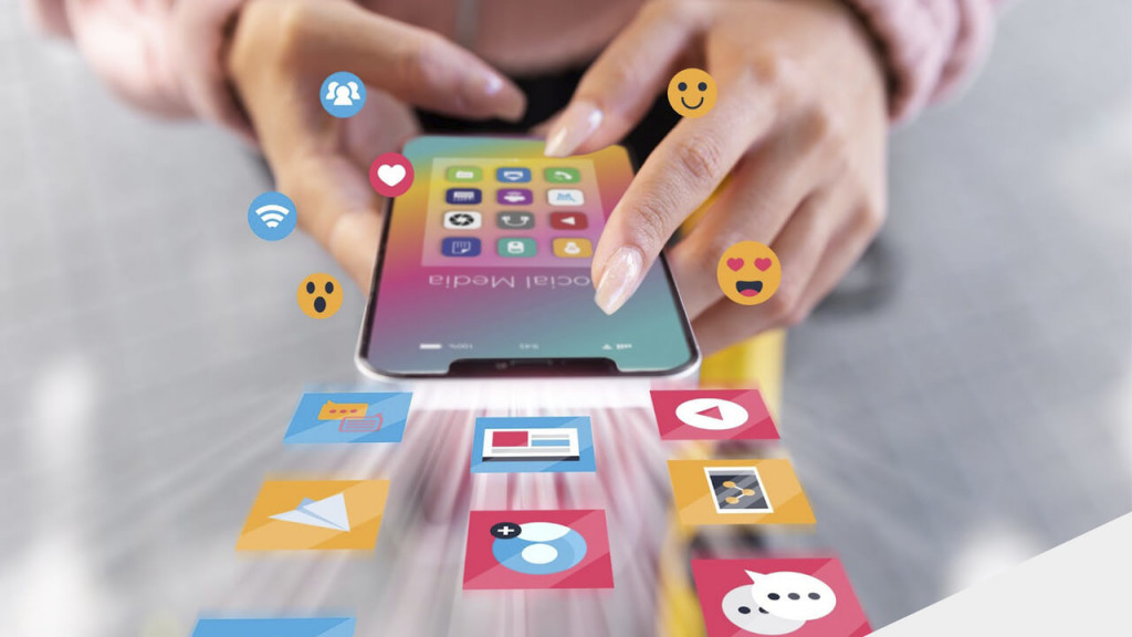 Duas mãos segurando celular com diversos aplicativos de mídias sociais. Vetores e ícones de compartilhamento, curtidas, apps e outros flutuam à sua volta.